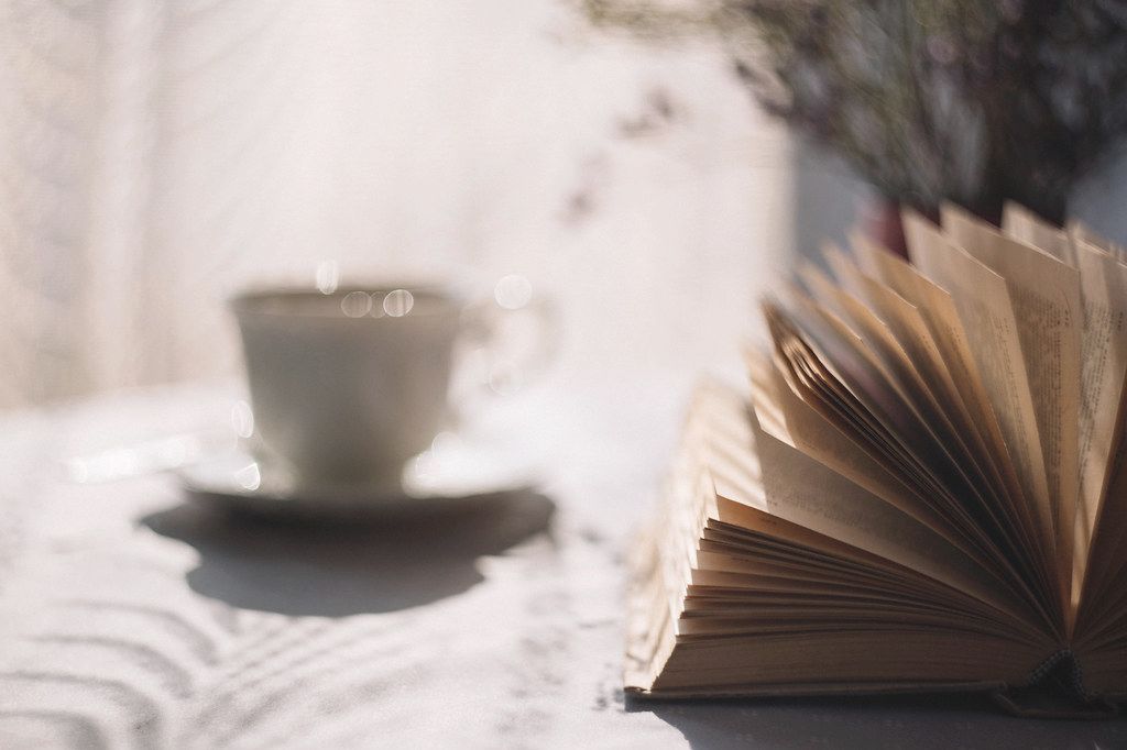 An open book and a cup of tea on a table in soft morning light.