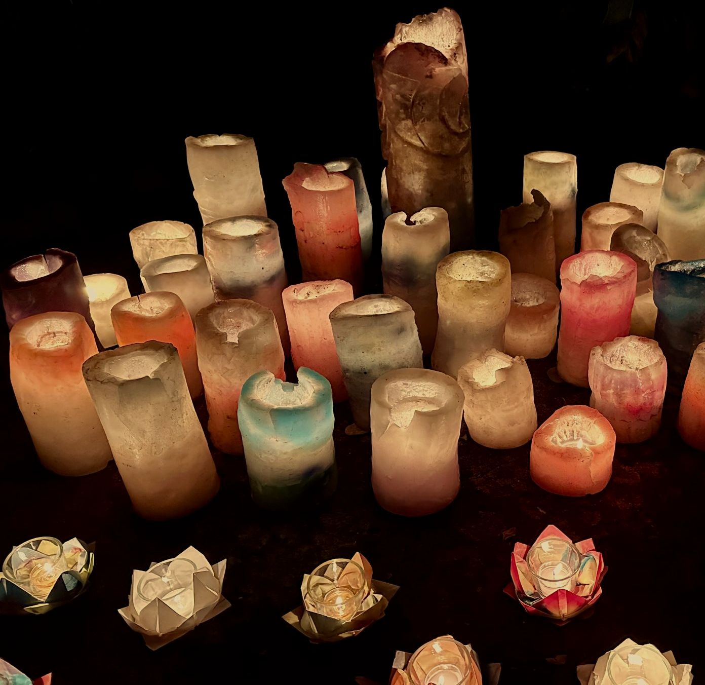 Dozens of lit candles of different shapes and sizes burning together in low amber light