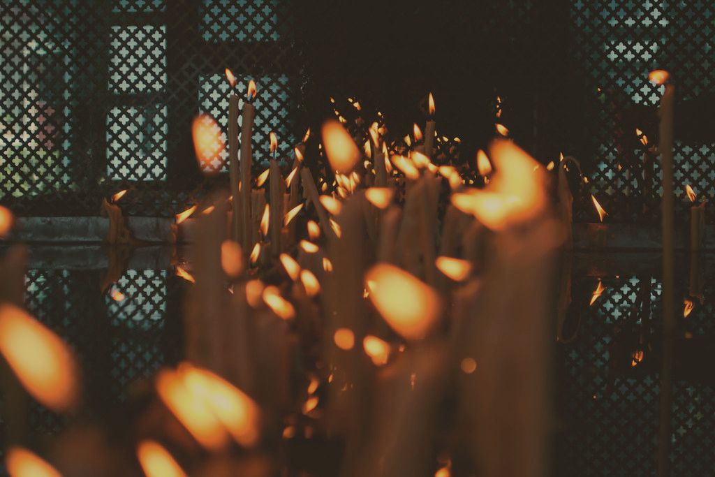 Dozens of slender candles burning together, amber flames against the dark