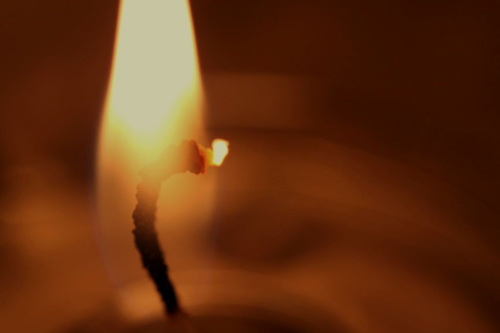 Close-up of a burning cotton wick, flame low and bright