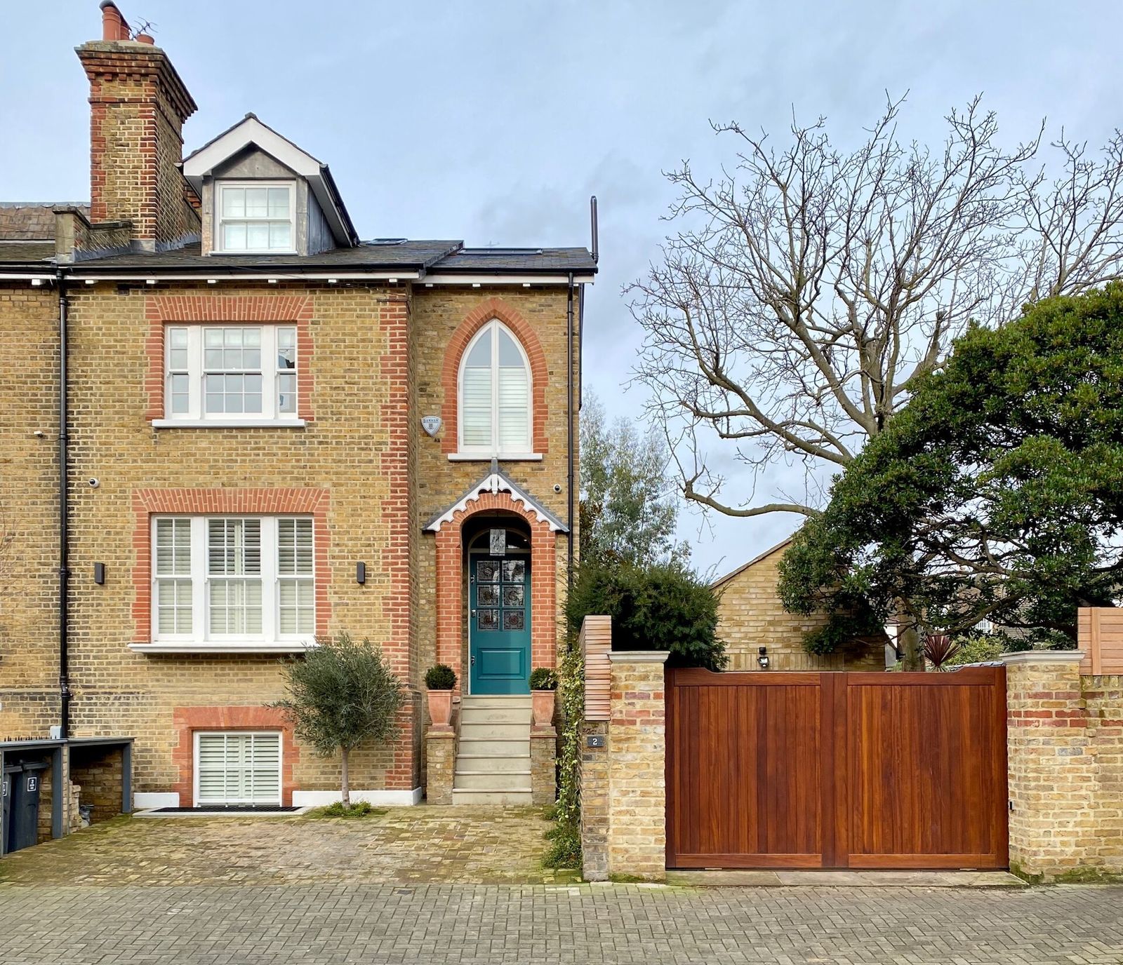 A London stock-brick Victorian house with red-brick window dressings, a teal front door and a paved front approach