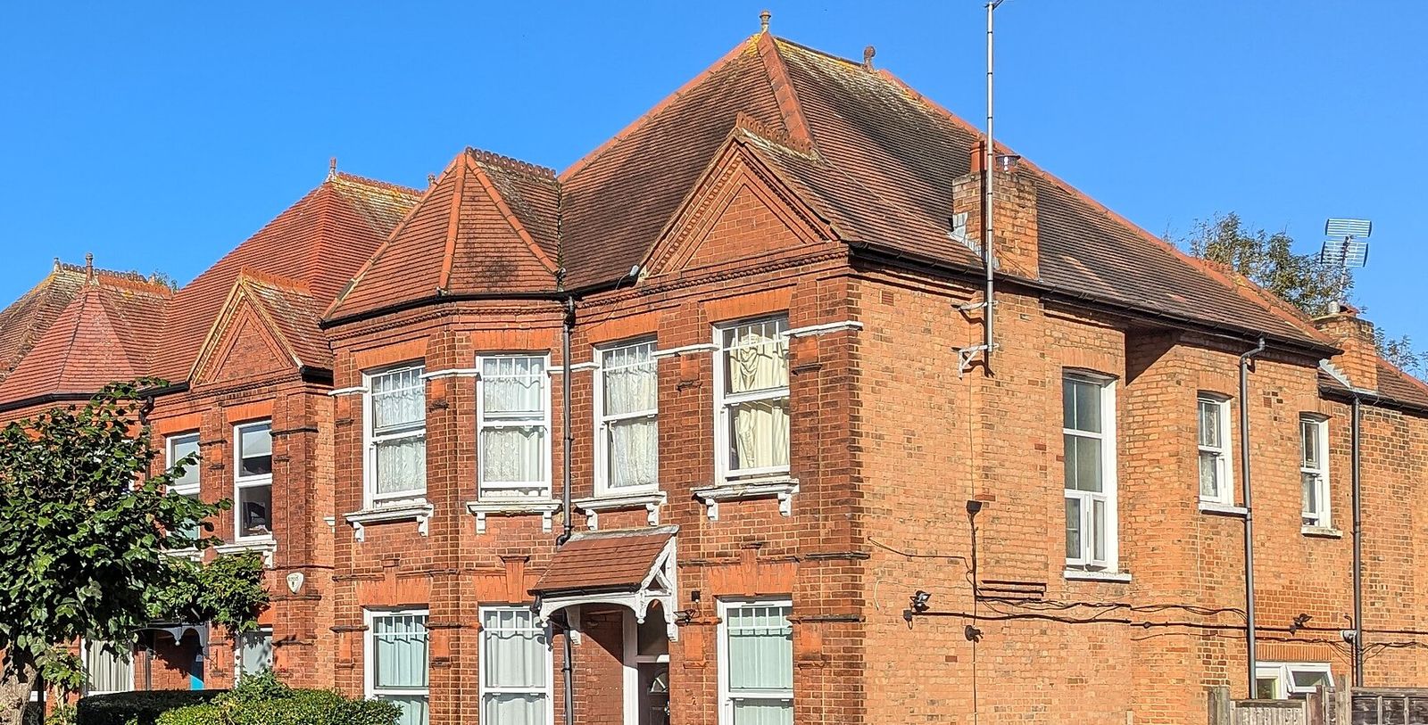Red-brick Victorian corner house with bay windows and sash frames on a sunny London street