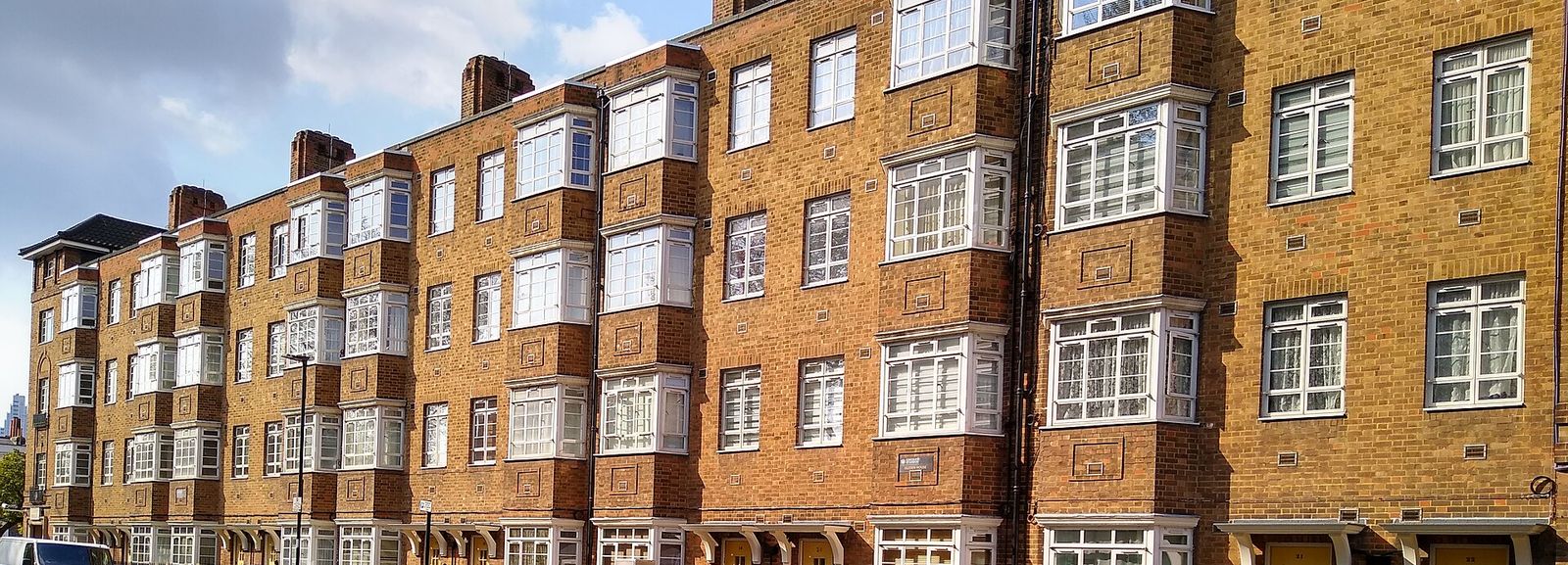Warm brick London mansion block with rows of white-framed bay windows in afternoon light