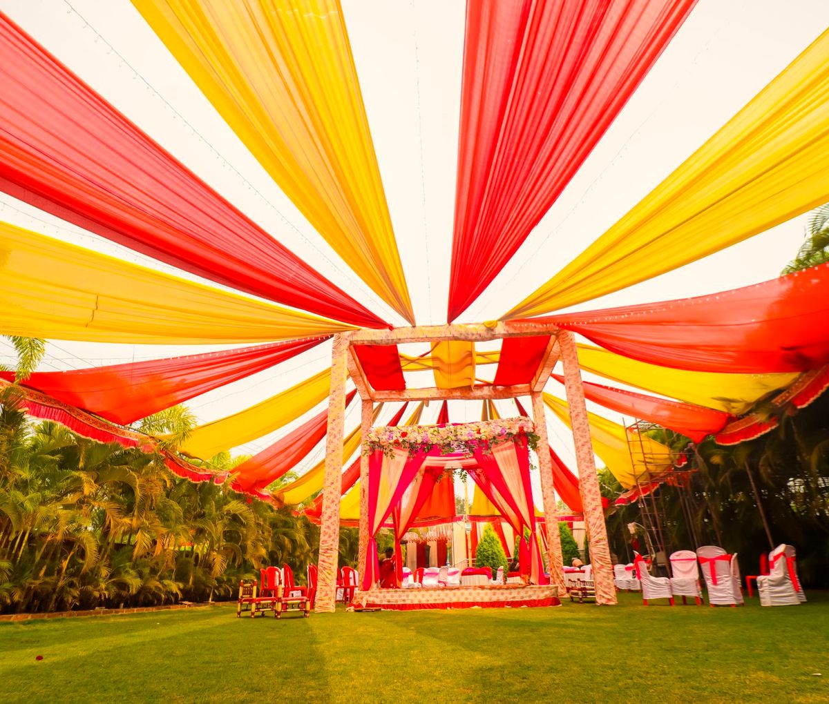 Outdoor wedding mandap beneath a canopy of red and marigold drapes