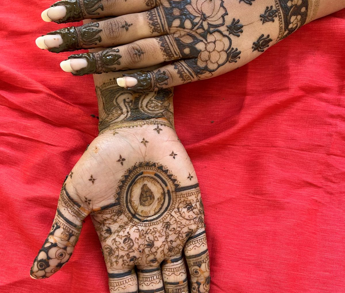 Hands resting on a red cloth, covered in fresh mehendi designs