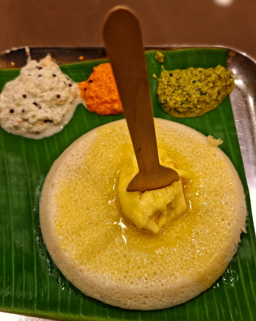 Butter idli topped with ghee on a banana leaf, with three chutneys alongside