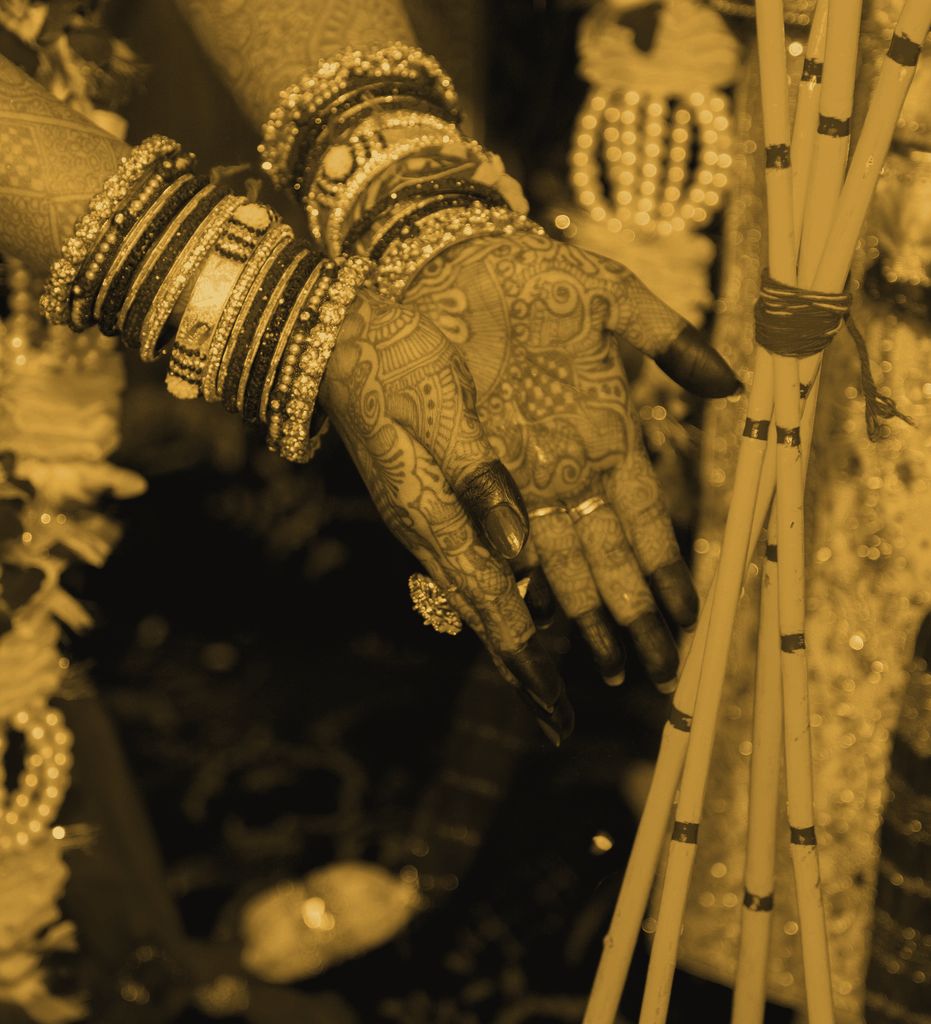 A bride’s hands covered in fresh mehndi, stacked with bangles, resting beside ceremonial sticks