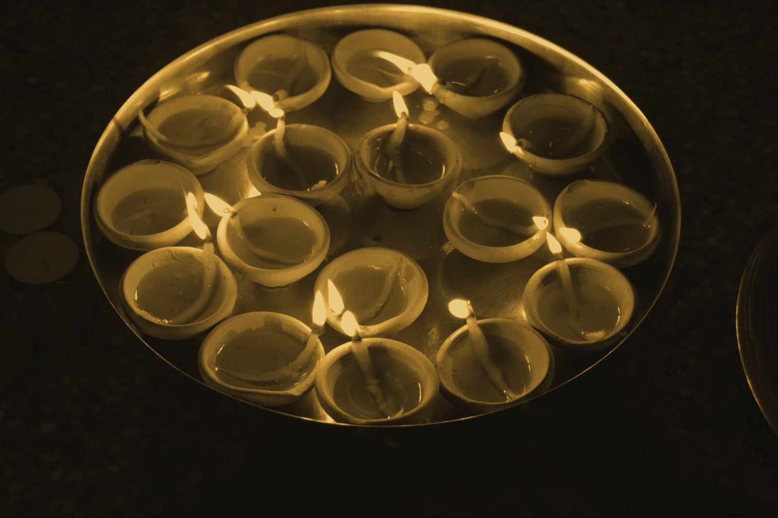A brass platter of lit clay diyas glowing in the dark