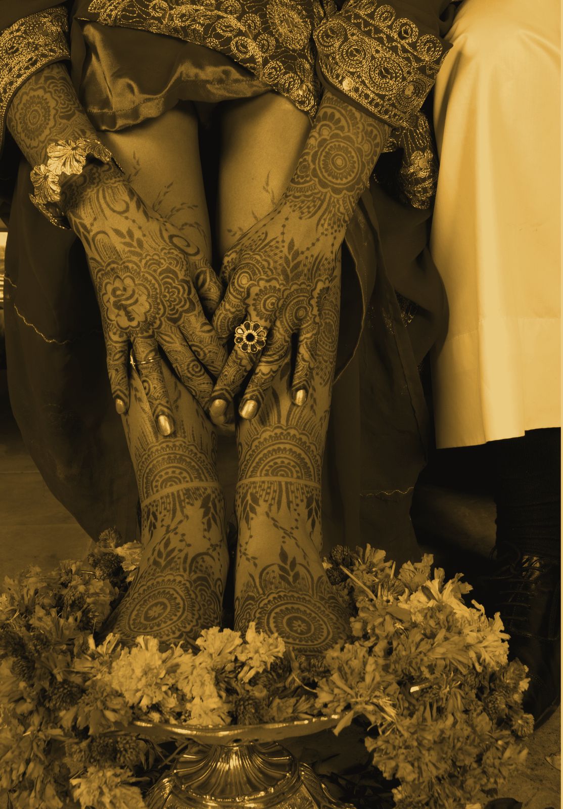 A bride’s mehndi-covered hands resting on her feet above a bowl ringed with marigolds