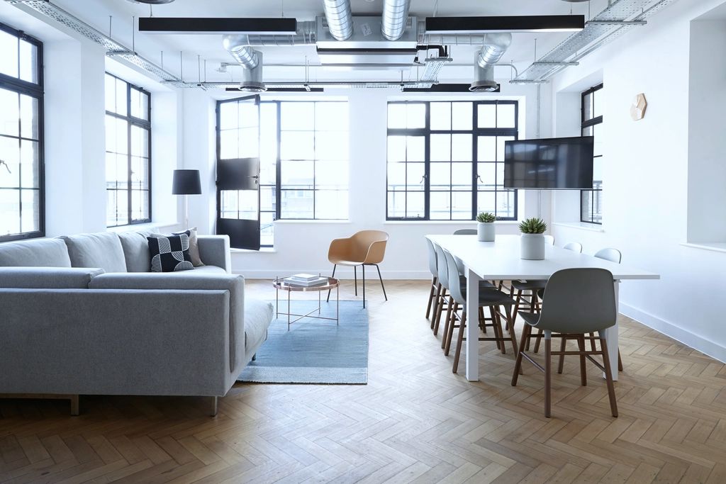 Bright loft office with black steel-framed windows, a long white table with chairs and a herringbone wood floor