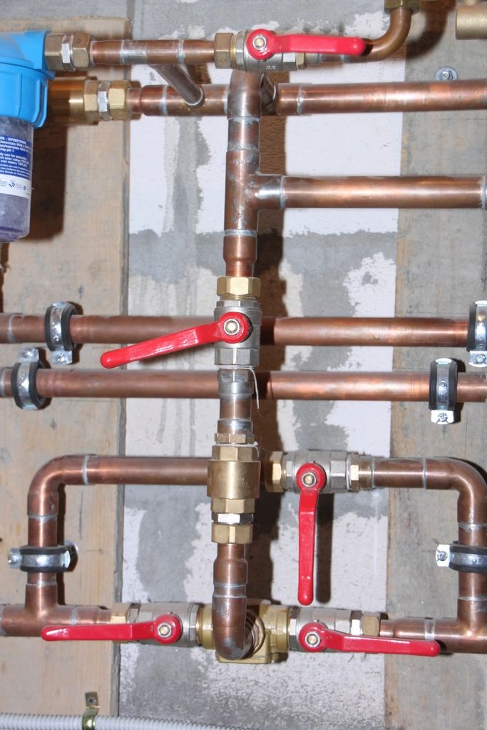 Copper heating pipework with red lever isolation valves, clipped to a workshop wall
